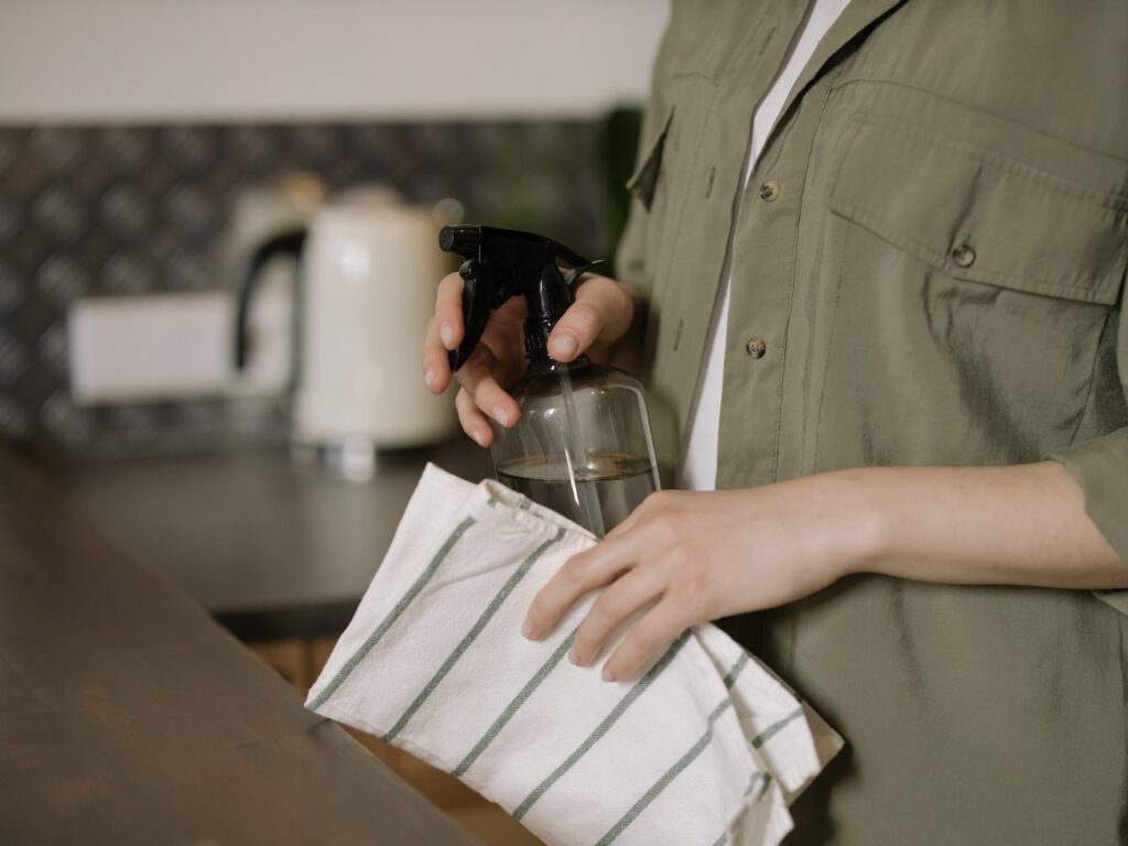 A person holding a spray bottle and cloth in a kitchen