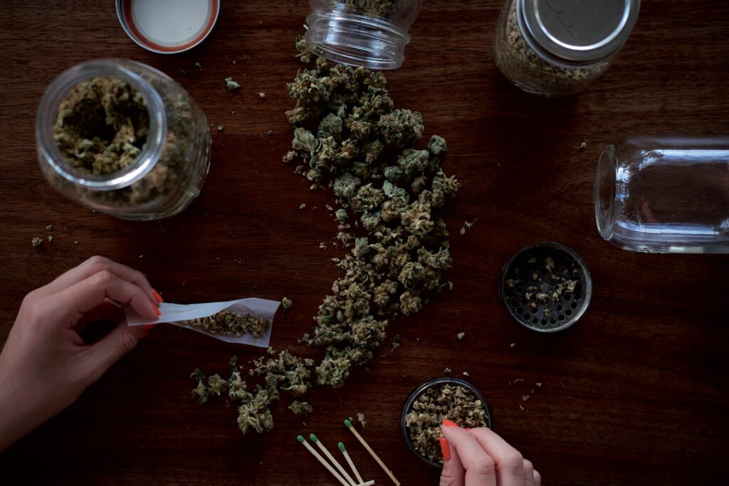 several jars of cannabis and a grinder assisting a woman rolling a joint