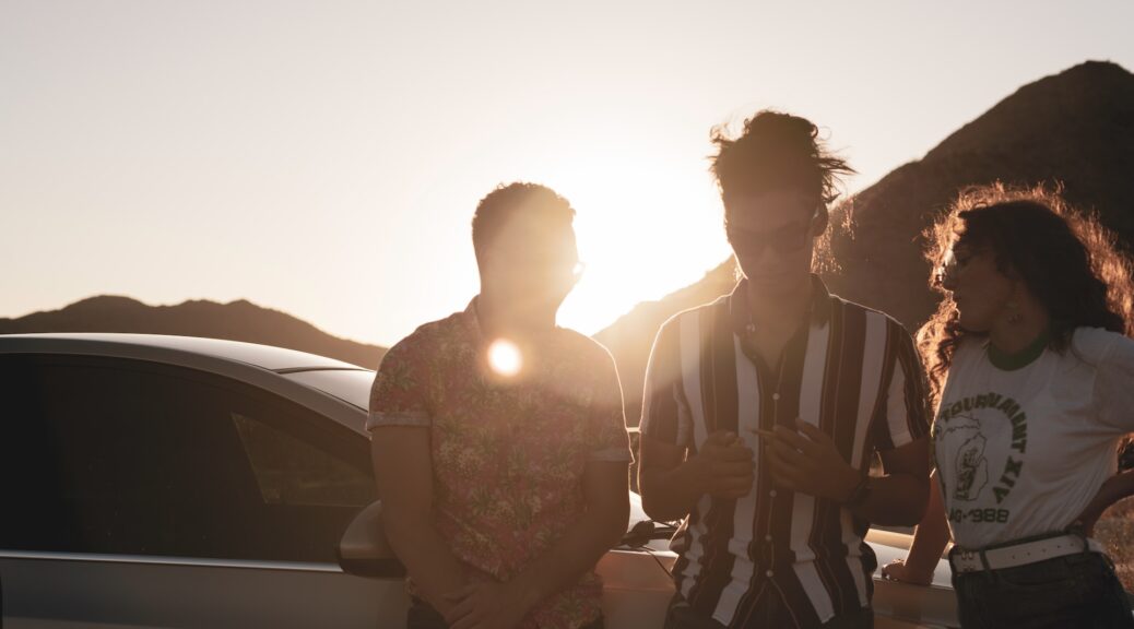 a group of two men and one woman about to light up and share a joint with the sunset in the background